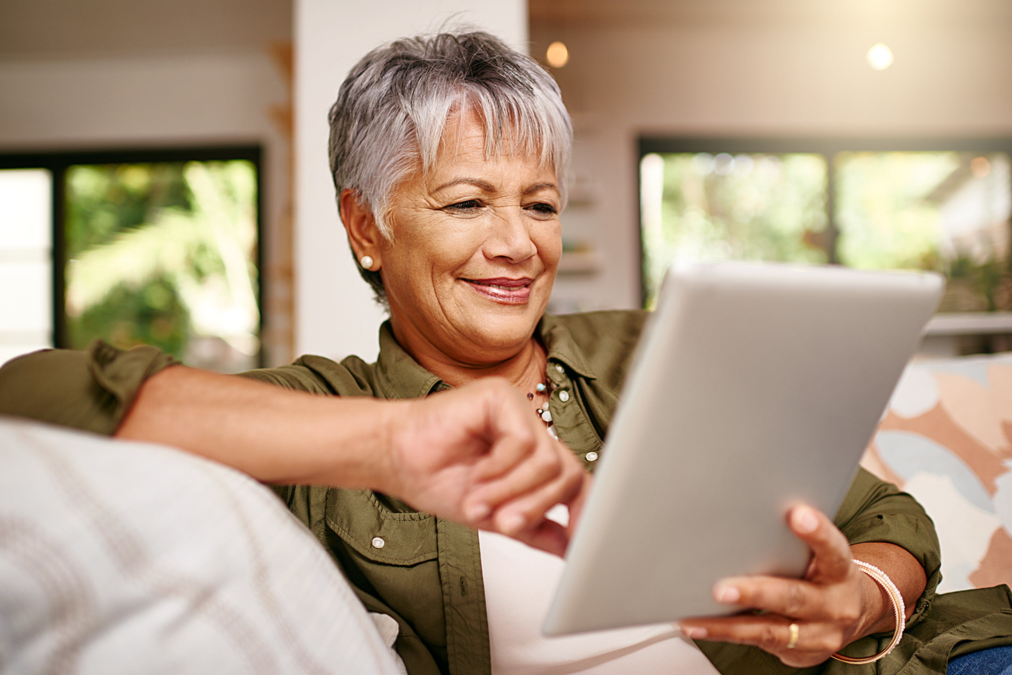 Older woman using tablet on a couch.